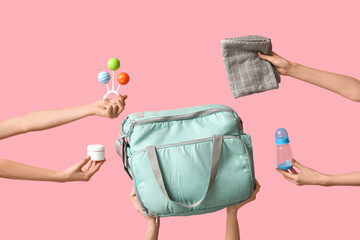 Many female hands with maternity hospital bag and baby things on pink background