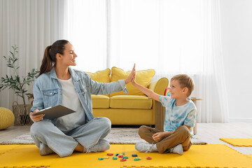 Female speech therapist with little boy giving each other high-five in office
