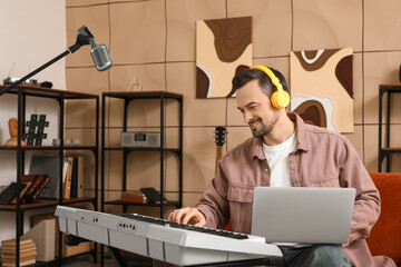 Young happy male composer with laptop while playing synthesizer in music studio