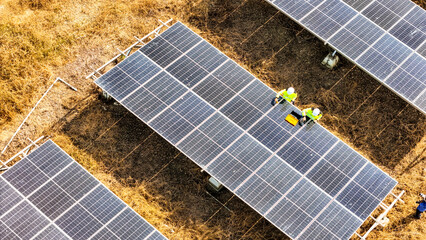 Two workers in safety gear performing maintenance under solar panels in a field, highlighting...