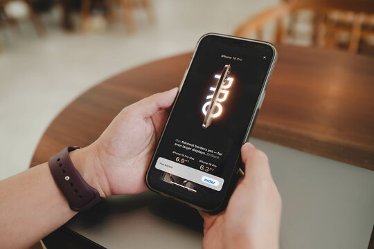 Bangkok, Thailand. May 27, 2025; Smartphone screen displaying iPhone 16 Pro order page with pricing and size options in a cafe environment with laptop in background.