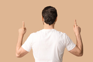 Young man pointing up on beige background, back view