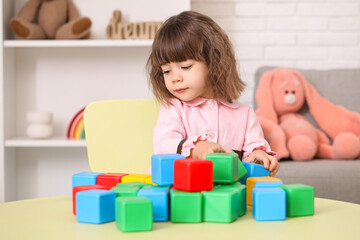 Cute little girl with plastic cubes at table in children's room