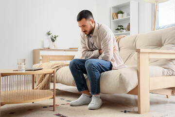 Young man suffering from bellyache on sofa at home