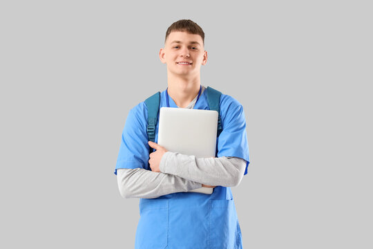 Male medical intern with laptop on light background