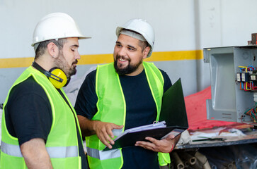 One smiling male factory or industrial worker showing how to use a machine or equipment to another...
