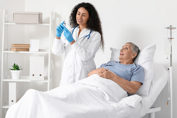 Fototapeta premium Female African-American doctor giving injection to senior patient in hospital room