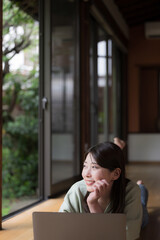 和風の古民家の縁側で寝転がってパソコンをする女性　田舎でのリモートワークや地方移住のイメージ　縦