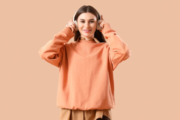 Beautiful young woman in headphones on beige background