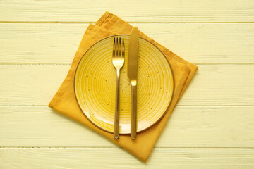 Beautiful table setting with golden cutlery on yellow wooden background
