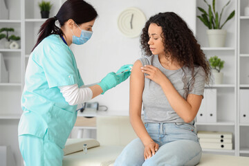 Female doctor vaccinating African-American woman in clinic