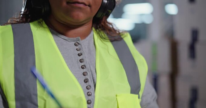 Close-up of the face and hands of a woman standing in a warehouse taking notes on a clipboard.