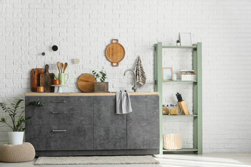 Counters with sink and utensils near white brick wall in kitchen interior
