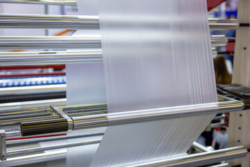 Industrial production of polymer packaging film. Pulling the film through the chrome-plated rollers of a production machine. Factory for the production of packaging materials and plastics