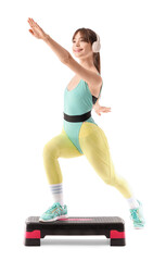 Sporty young woman in headphones exercising on aerobic stepper against white background