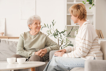 Senior woman with her daughter sitting on sofa at home. Mother's Day celebration