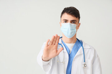 Male doctor in medical mask showing stop gesture on light background
