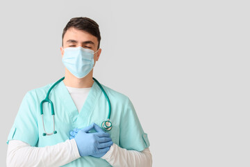 Male nurse in medical mask keeping his hands on heart against light background