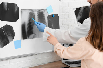 Male doctor showing x-ray scan of lungs on magnetic board to woman in clinic, back view
