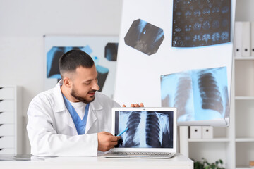 Male doctor showing x-ray scan of lungs on laptop at table in clinic