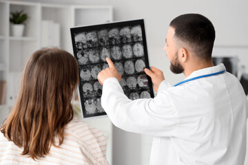 Fototapeta premium Male doctor showing MRI scan of head to woman in clinic, back view