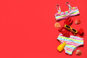 Composition with children's swimsuit, seashells and beach sand molds on red background