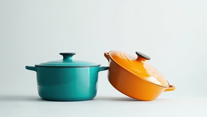 Two colorful enamel cookware pots, teal and orange, on a light background