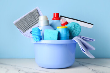 Bowl with cleaning supplies and bottles of detergent on blue background