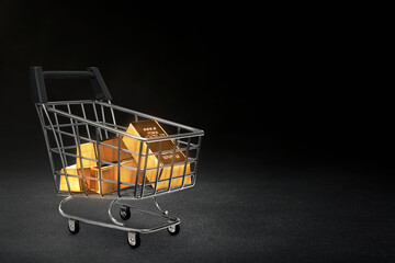 Stack of shiny gold bars in shopping cart isolated on dark background