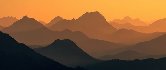 Sunset silhouettes of layered mountains fading into an orange sky
