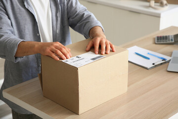 Male seller packing parcel for client at table in warehouse, closeup