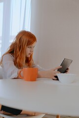 A 13-year-old teenage girl is having breakfast while playing on her tablet. She enjoys her morning...