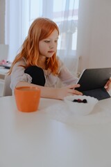 A 13-year-old teenage girl is having breakfast while playing on her tablet. She enjoys her morning...
