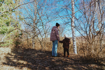 Fototapeta premium A mother and her 3-year-old daughter walk together in the park, enjoying nature and quality family time. A heartwarming moment of love, care, and happiness as they explore the outdoors together