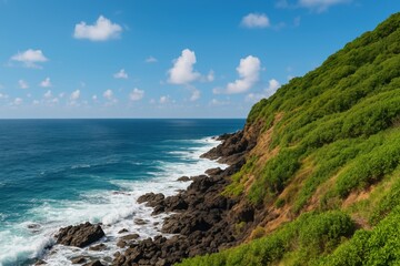 Fototapeta premium Scenic coastal view with lush green hills, rocky shoreline, and vibrant blue ocean under a bright sky with fluffy white clouds