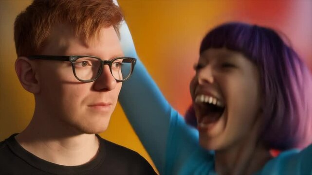 A man with short red hair and glasses wearing black and a woman with a purple-pink bob haircut and bangs