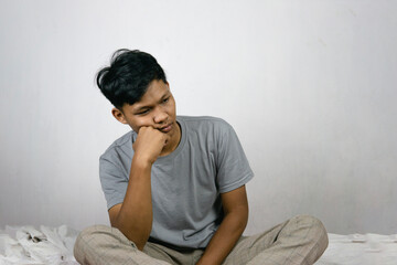 Portrait Of Depressed Young Indonesian Man Sitting On Bed At Home, Suffering Life Problems Or Mental Breakdown, Feeling Despair, Copy Space