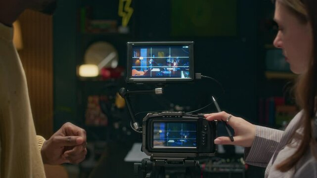 Medium close up shot of female Caucasian technician talking to male African American podcast host when setting camera before recording in studio