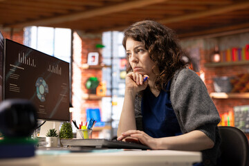 Young company analyst at office watching business presentation on PC display, reviewing statistics charts and performance metrics. Employee looking at presentation graphs on computer.