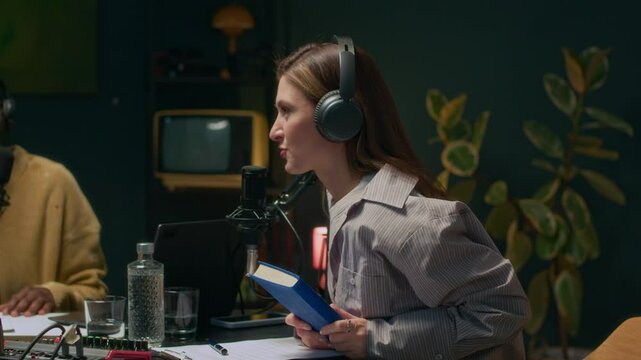 Handheld shot of female Caucasian podcaster accepting book as present from mature writer during audio interview recording with black male colleague