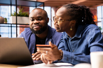 Mature couple managing online banking and payments with the credit card, entering digits on a website to confirm the money transfer. Casual people at home office makes transactions.