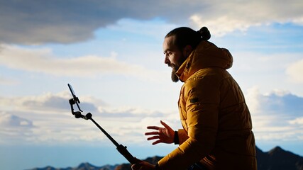 Content creator records a vlog in the mountains sharing his outdoor adventure with his audience. Male hiker always connected with a smartphone mounted on a stabilizing tripod. Camera B.