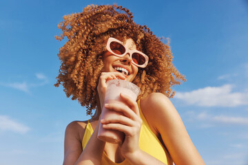 Fototapeta na wymiar Cheerful young woman enjoying a smoothie against a bright blue sky