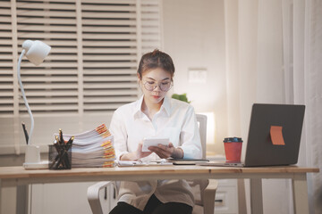 Asian businesswoman working late at night in office, reviewing documents under desk lamp, showing dedication, focus, and professional diligence.