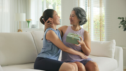 May Mother's day young adult child arm around cuddle hug give gift box to mature middle age old mum. Love kiss care mom asia elder people sit at home sofa happy smile enjoy family good time aging life © ChayTee