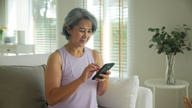 Asia adult people middle age happy relax old woman using mobile ask AI chatGPT chat bot look health care app sit at home sofa elder aging asian aged female. Online social media smart pay order system.