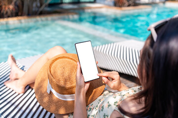 Young woman tourist using smart phone at resort pool while traveling for summer vacation