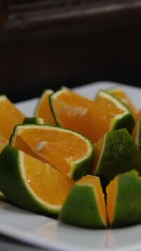 orange slices green Vietnamese oranges citrus fruits hanging on a branch, surrounded by glossy leaves. Captured outdoors in natural light, highlighting the vibrant and fresh details