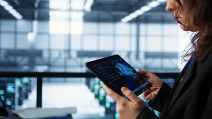 Engineer in data center with tablet integrating AI driven automation tools. Worker ensuring...