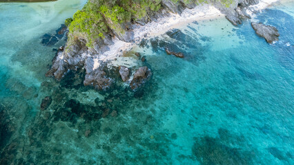The serene seascape of Okinawa showcases crystal-clear waters, exposed rocky formations, and gentle waves lapping against the shore. © chayakorn